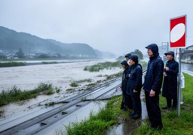 筑豊地域の雨に濡れた河川堤防と防災標識を見つめる地域住民